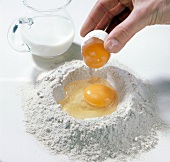 Eggs being added to flour on white background