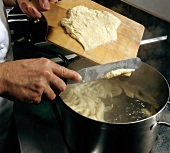Pizokel being prepared by adding dough to boiling water in pot