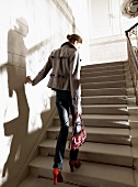 Frau geht eine Treppe hoch mit Wollhose, Wolljacke und roter Tasche