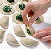 Stuffed dough slices being folded into half moon shape