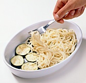 Layer of spaghetti being spread on eggplant slices in baking dish