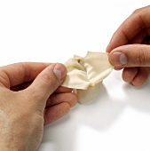 Close-up of hands holding stuffed pasta edges while preparing won-tans, step 4