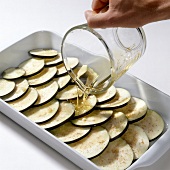Oil poured over eggplant slices in baking tray while preparing macaroni casserole, step 1