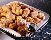 Sugared apple walnut fritters with icing and tongs on silver plate