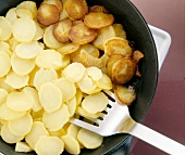Sliced boiled potatoes and fried potatoes turned with spatula in skillet pan