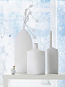 Various matt white vases on table in front of transparent curtain