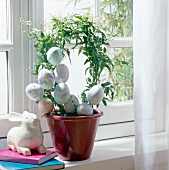 Easter bunny beside plant wreath with colourful Easter eggs in flower pot on window sill