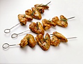 Crispy chicken skewers garnished with rosemary on white background