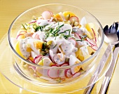Potato salad with egg, radishes cucumber, chives and salad dressing in glass bowl