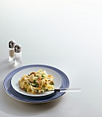 Vegetable pasta on plate beside salt and pepper shakers on white background