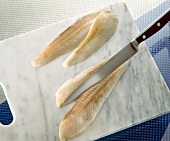 Close-up of plaice fillets cut in half with a knife on white chopping board