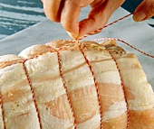 Close-up of woman's hands making node at the end of the wrapped roast