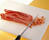 Close-up of raw ham being cut with a knife into cubes