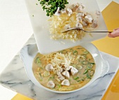 Close-up of mushrooms, cheese and chive added to scrambled eggs in bowl