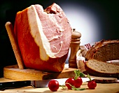 Close-up of ham on wooden board, bread, radishes, pepper mill and one messer