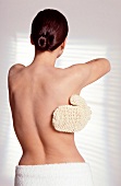 Rear view of semi nude woman massaging her back with sisal glove