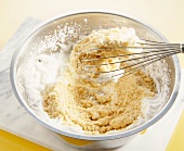 Almonds, breadcrumbs and egg whites in bowl with whisk