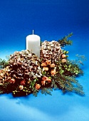 White candle in wreath decorated with various dried flowers on blue background
