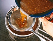 Gravy being poured through sieve for preparing veal breast