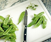 Sugar peas with knife on cutting board