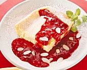 Close-up of pear pudding with almonds, fruit sauce and icing sugar on plate