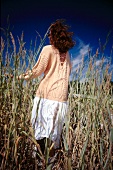 Rear view of woman wearing sweater walking through cornfield