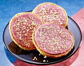 Three American pies with raspberry icing and chopped almonds on plate