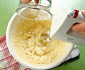 Mixing milk, oil and cream in bowl with mixer for making mayonnaise