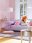 Lilac sofa and silver-leaf side table in living room with pink walls