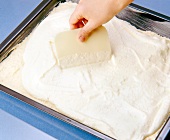 Cheese being spread with dough scraper on baking sheet