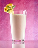 Glass of pineapple and coconut juice garnished with slice of pineapple and mint leaves