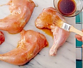 Chicken legs being prepared by applying mixture of red pepper powder and oil with brush