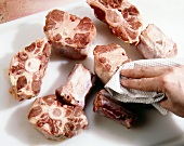 Close-up of oxtail pieces being pat dried with kitchen napkin to prepare oxtail stew