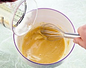 Oil being stirred with mustard, vinegar, salt and pepper in bowl