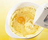 Egg yolk and dough being whisked with electric whisk