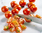 Tomatoes being cut into quarters with kitchen knife