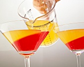 Juice being poured from jug in two glasses with campari jelly