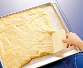 Rhubarb pie dough being spread with scraper on tray