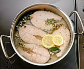 Gekochter Fisch, Zitronenscheiben und Gewürze im Kochtopf, close-up.