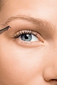Close-up of gray eyed woman sticking artificial eyelashes with eyelash tweezers