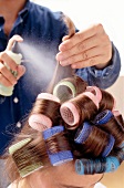 Curling spray being sprayed on woman's hair withy curlers