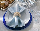 Tischdekoration: Serviettenring mit Muscheln und Schnecke, blauer Teller