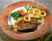 Steak mit Bohnenbündel und Zwiebelringen auf Teller