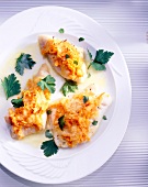 Cod fillets with carrots crust, cream sauce and parsley on plate