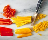 Red and yellow peppers being diced with kitchen knife