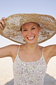 Jennifer Frau hält d. Sonnenhut am Kopf fest, fröhlich, am Strand