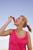 Side view of happy woman holding bunch of red currants near mouth