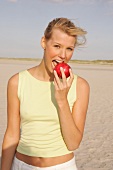Frau am Strand beißt in ihren roten Apfel