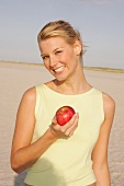 Jennifer Frau am Strand hält einen roten Apfel in der Hand, lacht