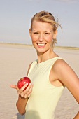 Frau am Strand steht seitlich mit e. Apfel in der Hand